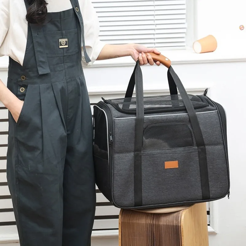 Grey folding pet carrier standing on a wooden stool, with a hand on its top handle
