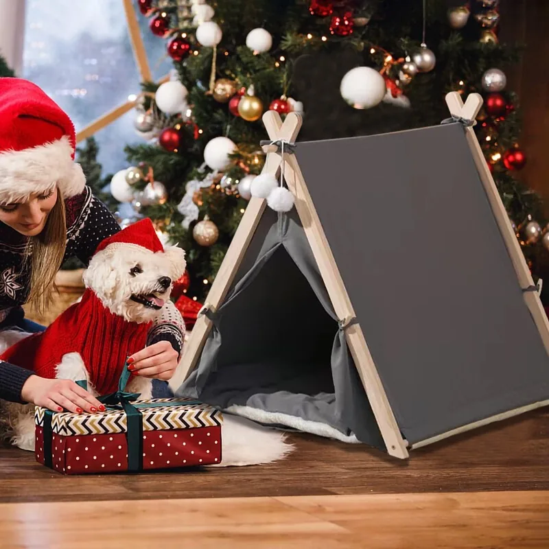 The grey teepee by a Christmas tree, with a small white dog in a Santa hat and a wrapped present beside it
